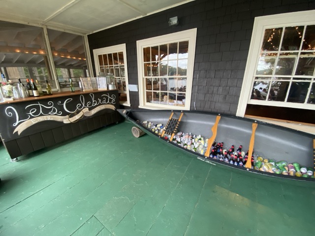 'Let's Celebrate' chalkboard bar at Camp Wigwam with a wooden canoe used as a drink cooler on the lakeside porch
