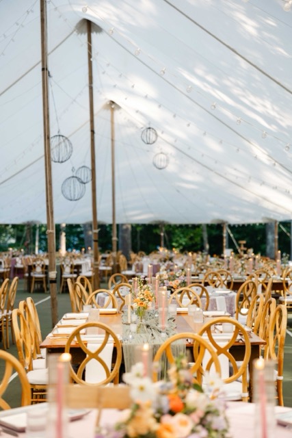 Sailcloth wedding tent at Camp Wigwam in Waterford, Maine, set with long farm tables, hanging lanterns, and pastel candlelight for a lakeside reception
