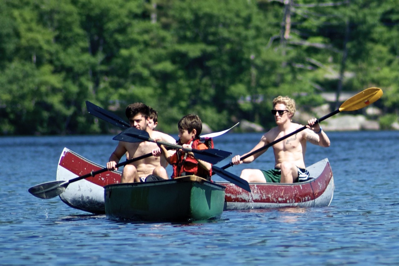 Counselors and a camper paddling canoes across calm Bear Lake on a sunny morning