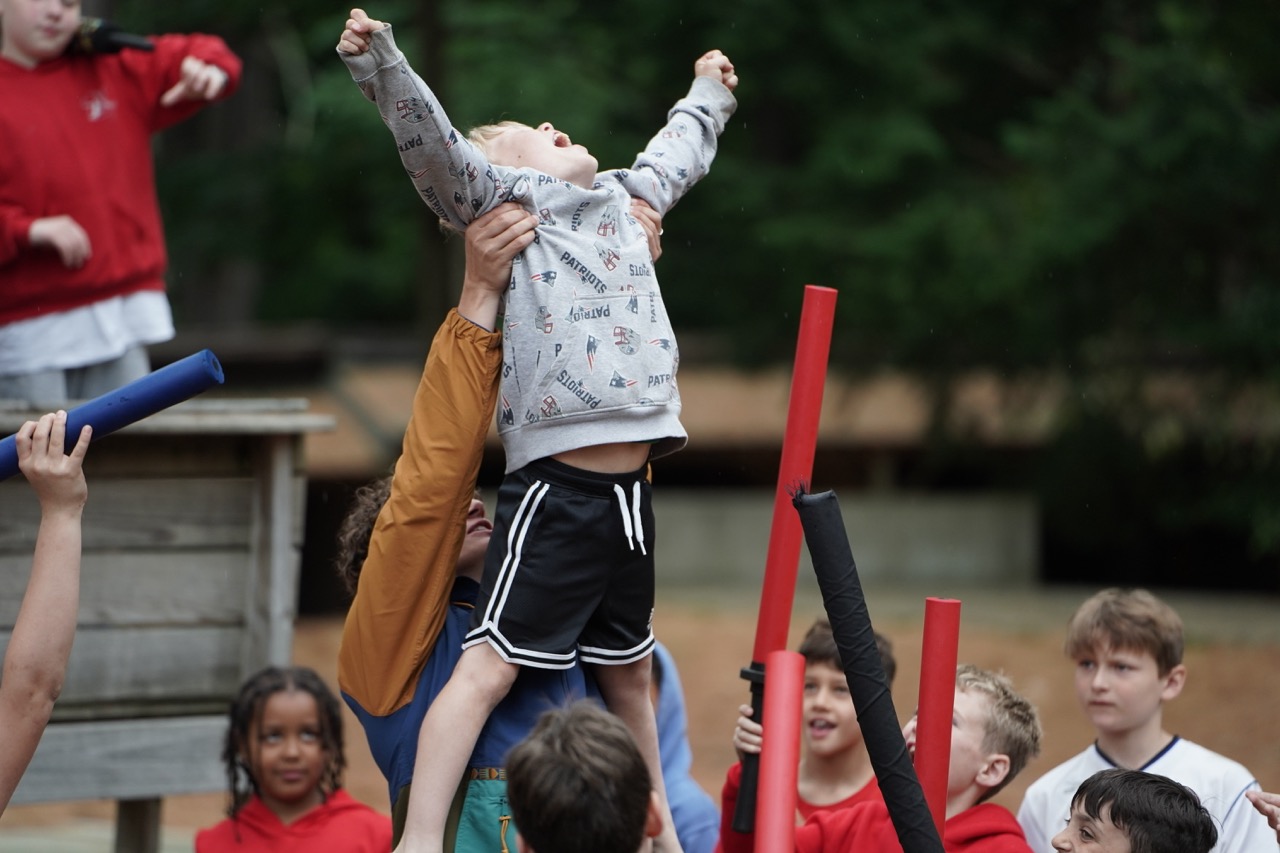 Camper hoisted into the air cheering during a spirited team game on the field