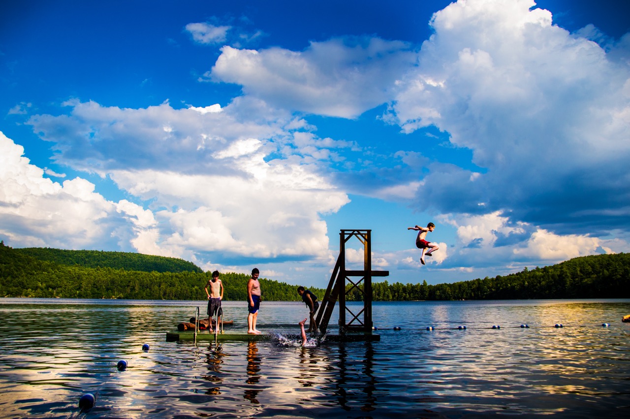 Camper leaping off the waterfront tower into Bear Lake on a sunny summer afternoon at Camp Wigwam