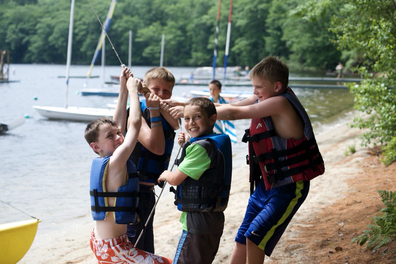 Four young campers in life jackets clowning around together on the sandy waterfront beach