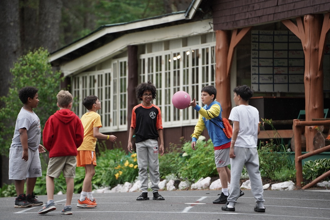 Group of campers playing a circle ball game on the blacktop outside the lodge