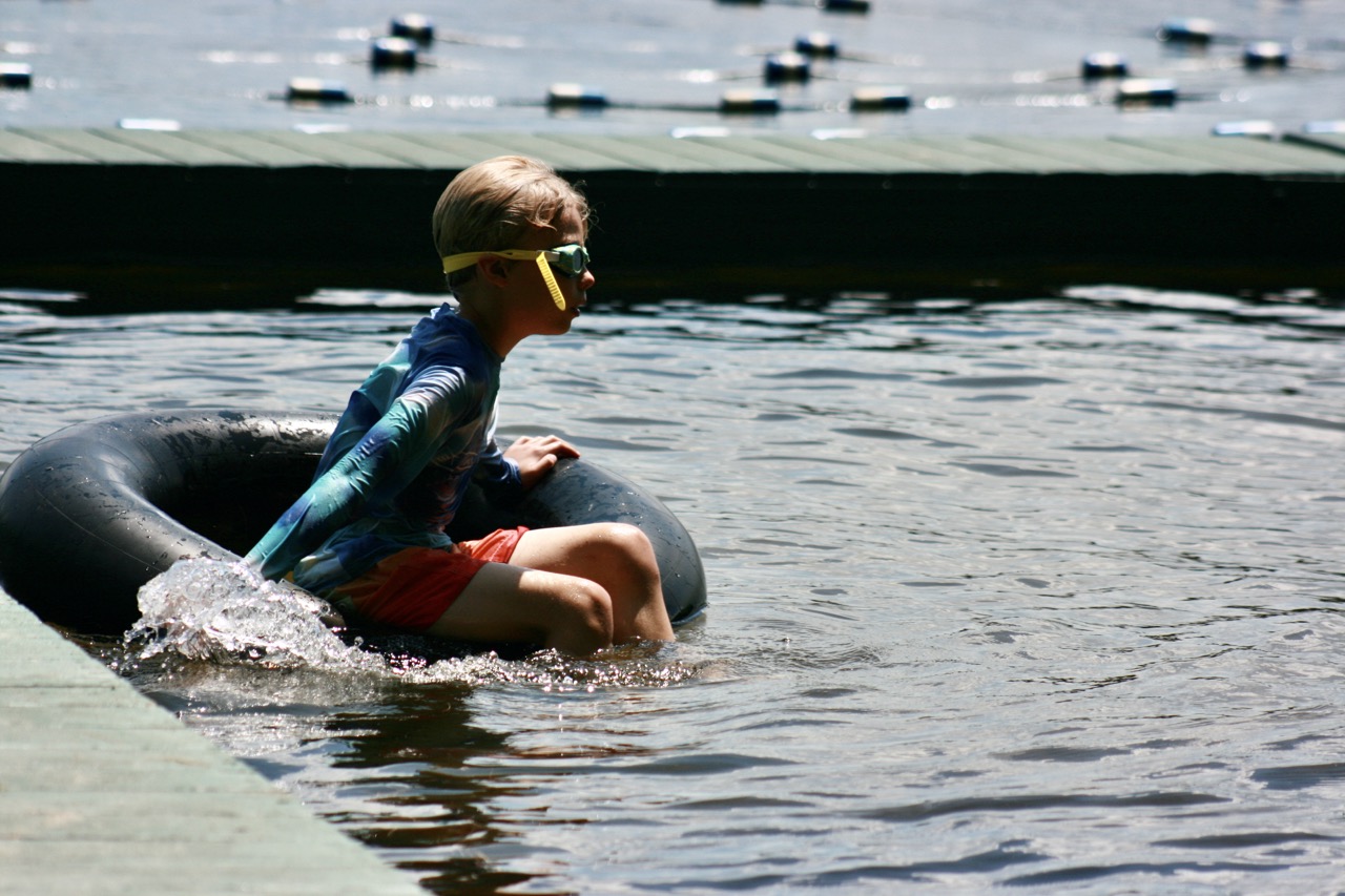 Camper in goggles floating in an inner tube along the waterfront swim docks at Bear Lake