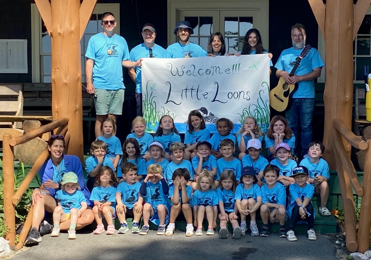 Little Loons campers and counselors gathered on the Wigwam Lodge porch with the Welcome Little Loons banner